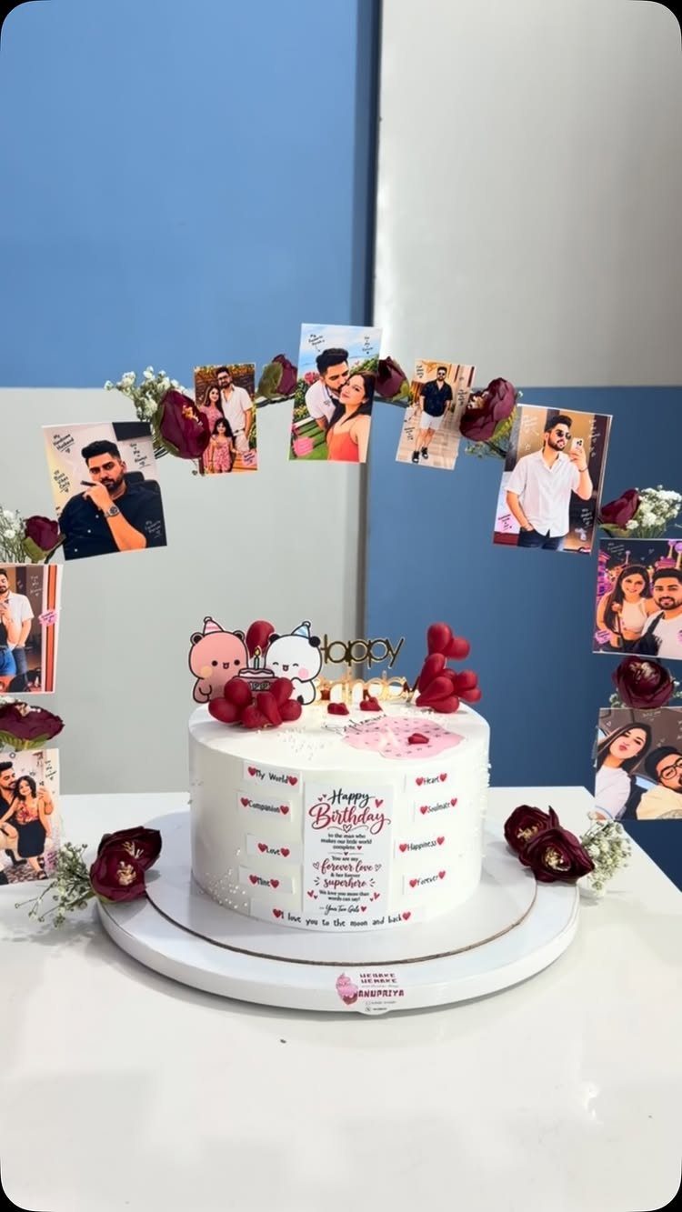 White birthday cake with red roses and cartoon figures on a photo backdrop.