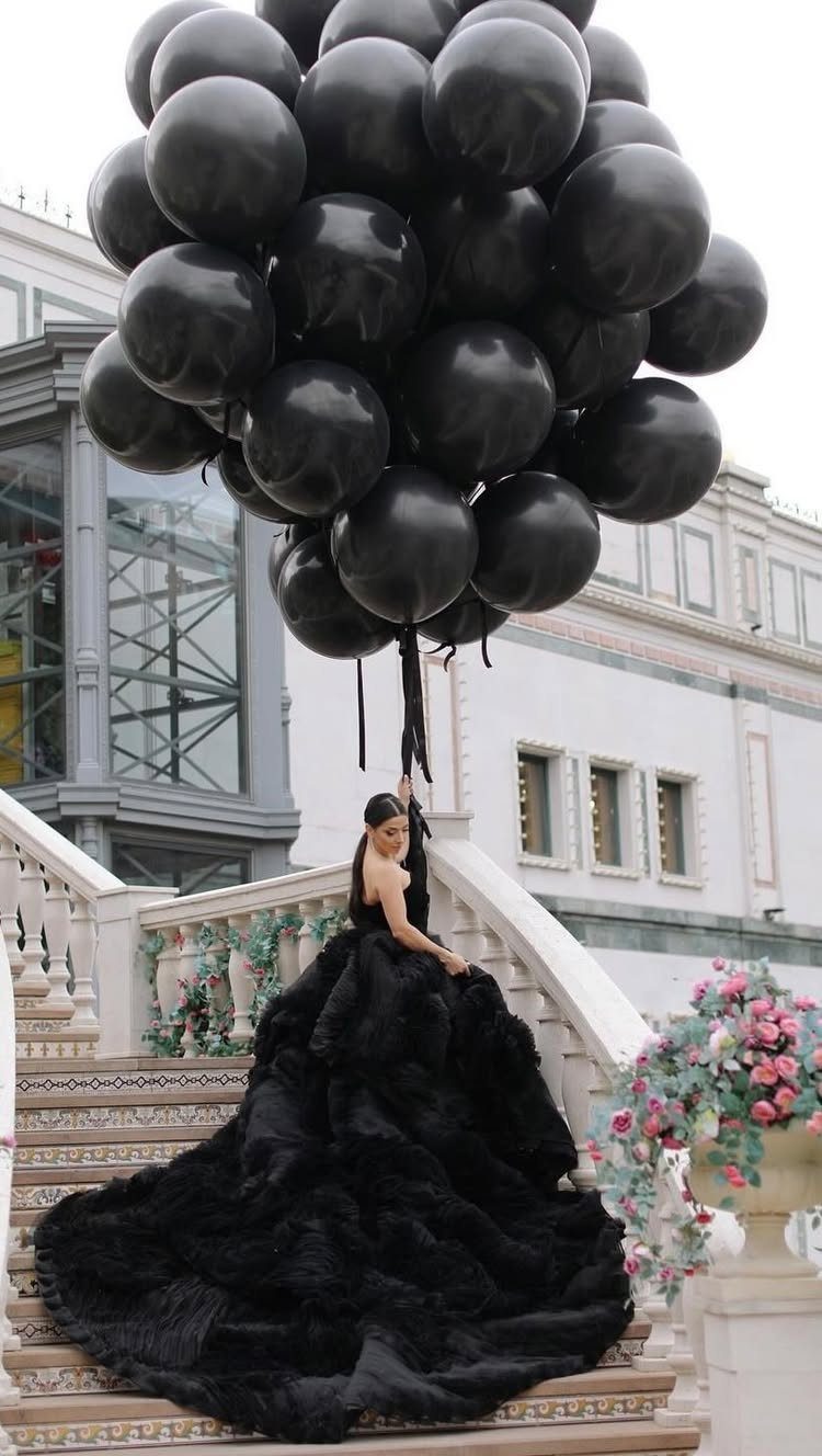 Woman in a black ruffled gown holding a large bunch of black balloons.