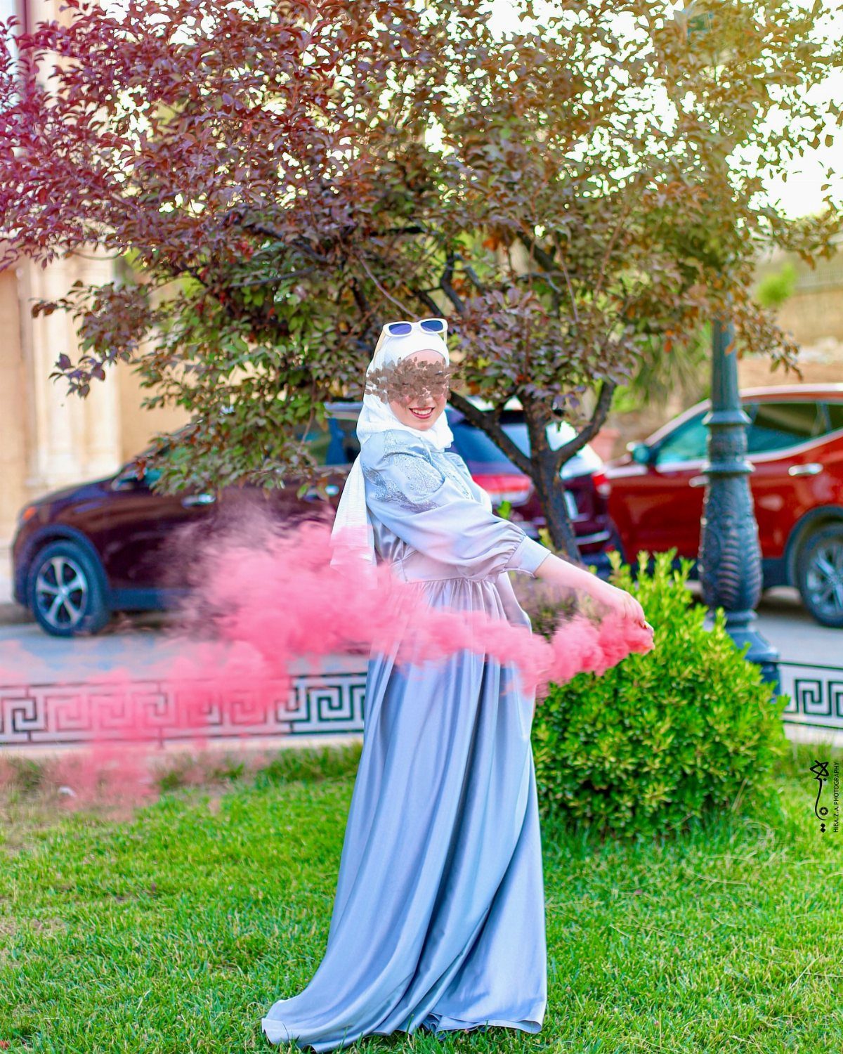 Woman in blue gown and hijab holding a pink smoke bomb outdoors.