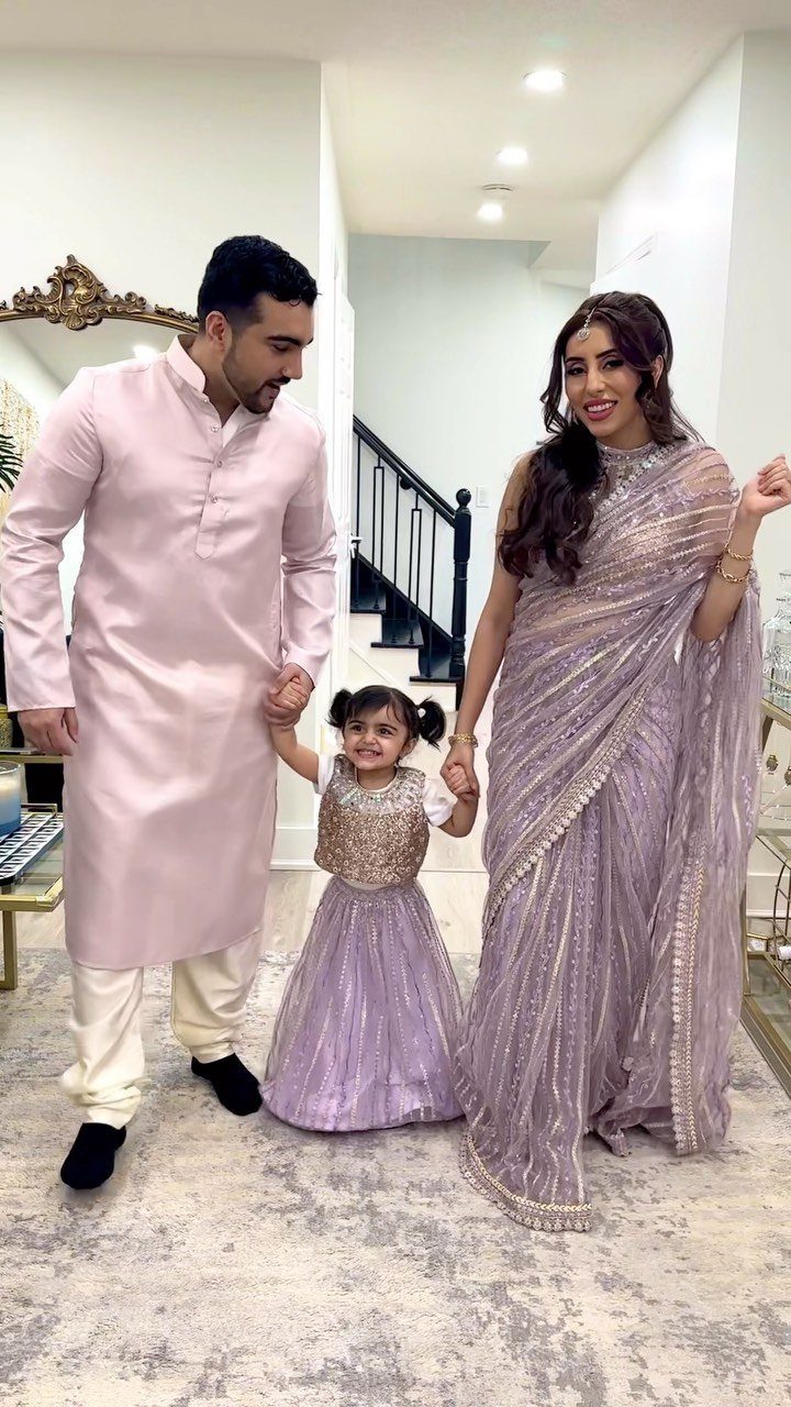 Family in coordinated lavender traditional South Asian clothing posing together in a bright room.