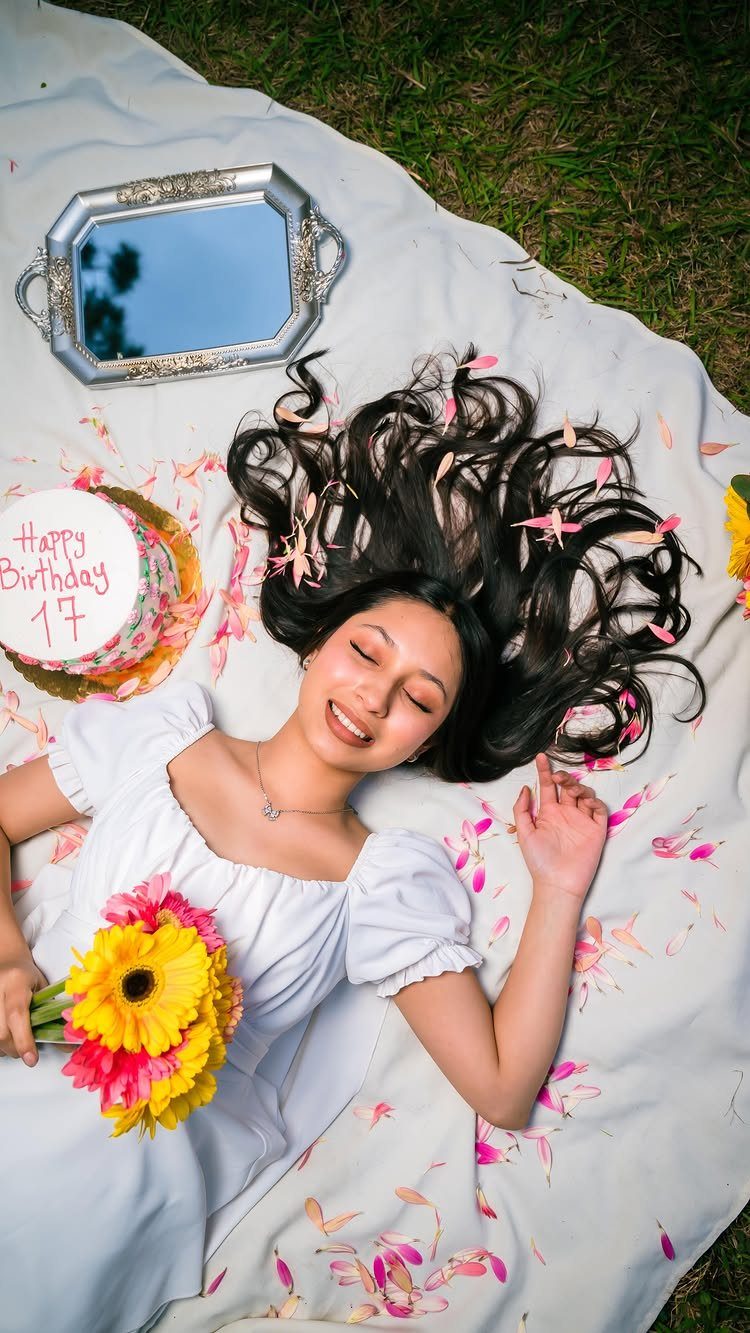 Woman in white dress lying on a picnic blanket with cake and flowers