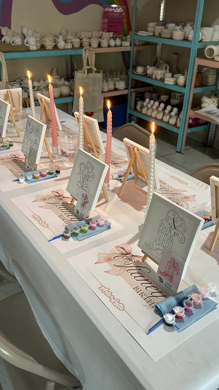 Painting party table setup with canvases, paint palettes, and lit candles in studio
