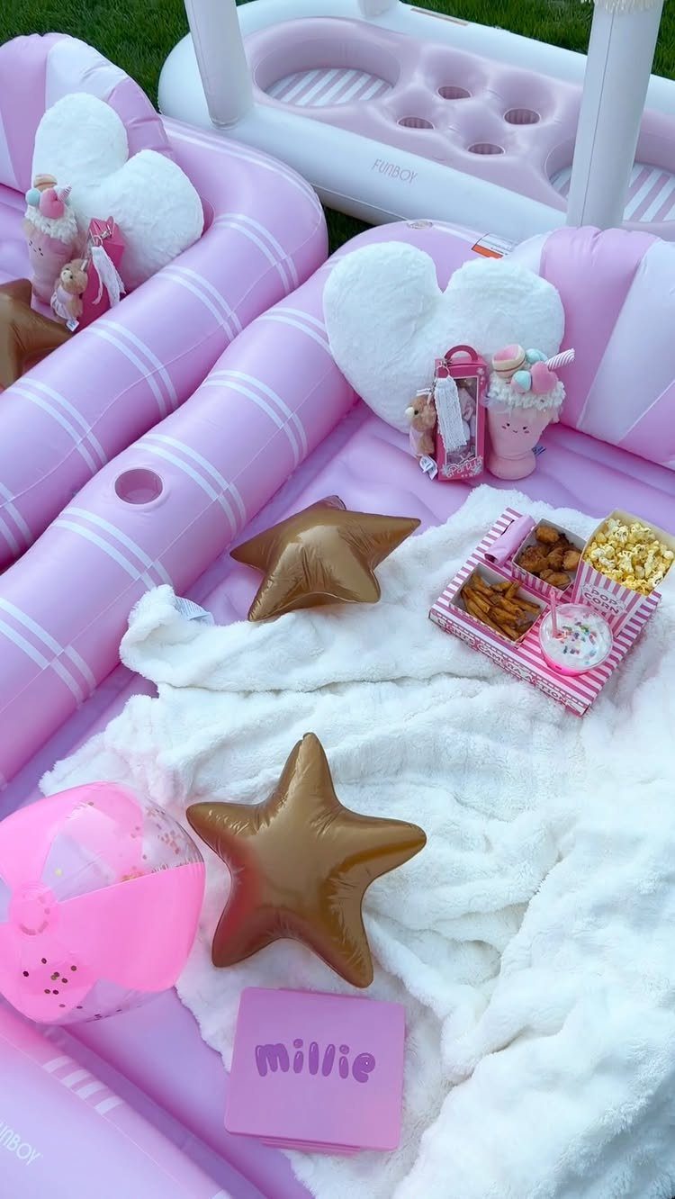 Pink inflatable pool filled with white blankets, gold star balloons, and party snacks.