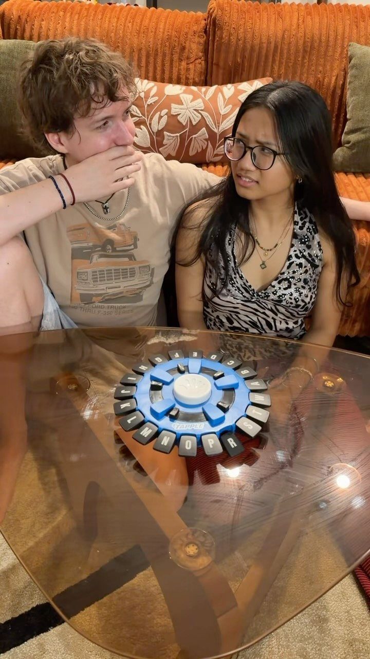 Two teenagers sitting on a sofa playing a board game on a glass table