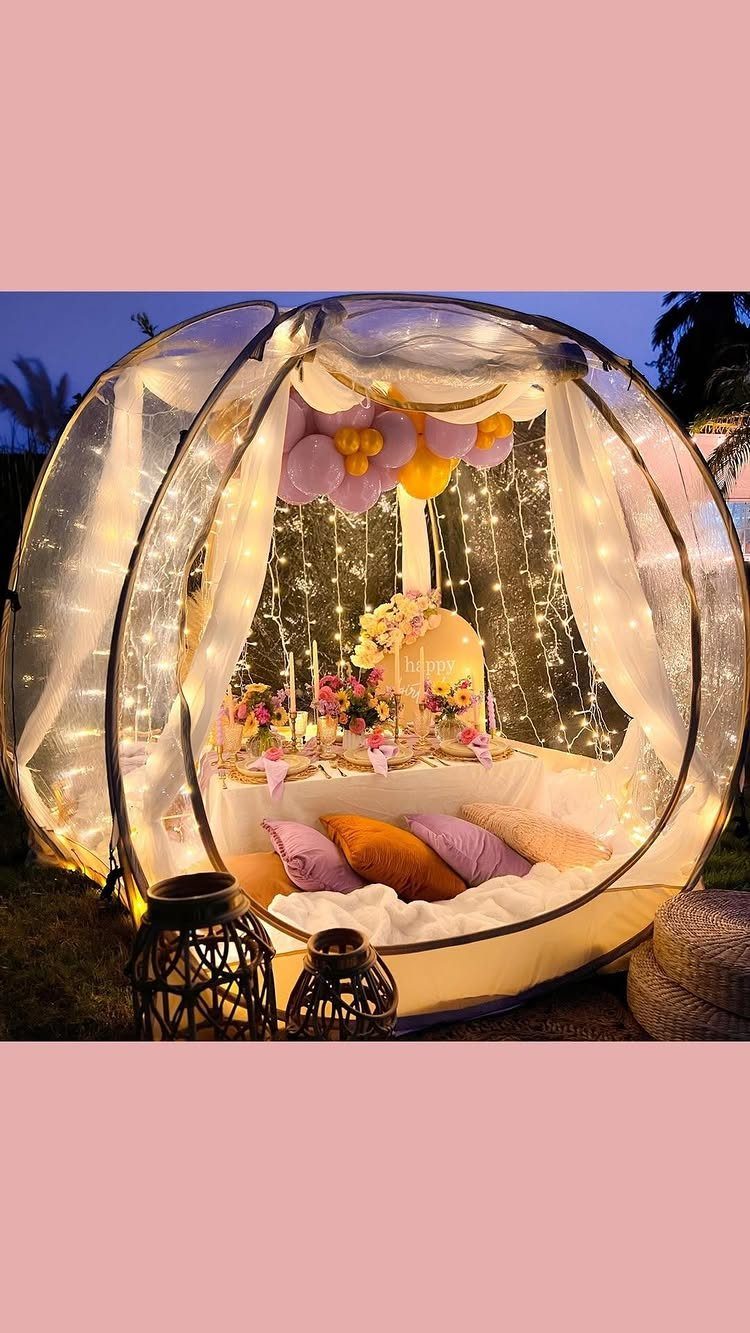 Transparent bubble tent with fairy lights, colorful pillows, and balloons for glamping.