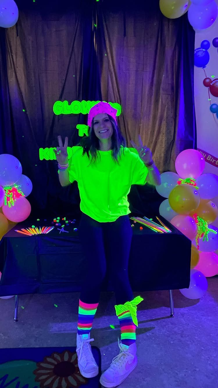 Young woman in neon clothing posing at a glow-in-the-dark party with balloons.