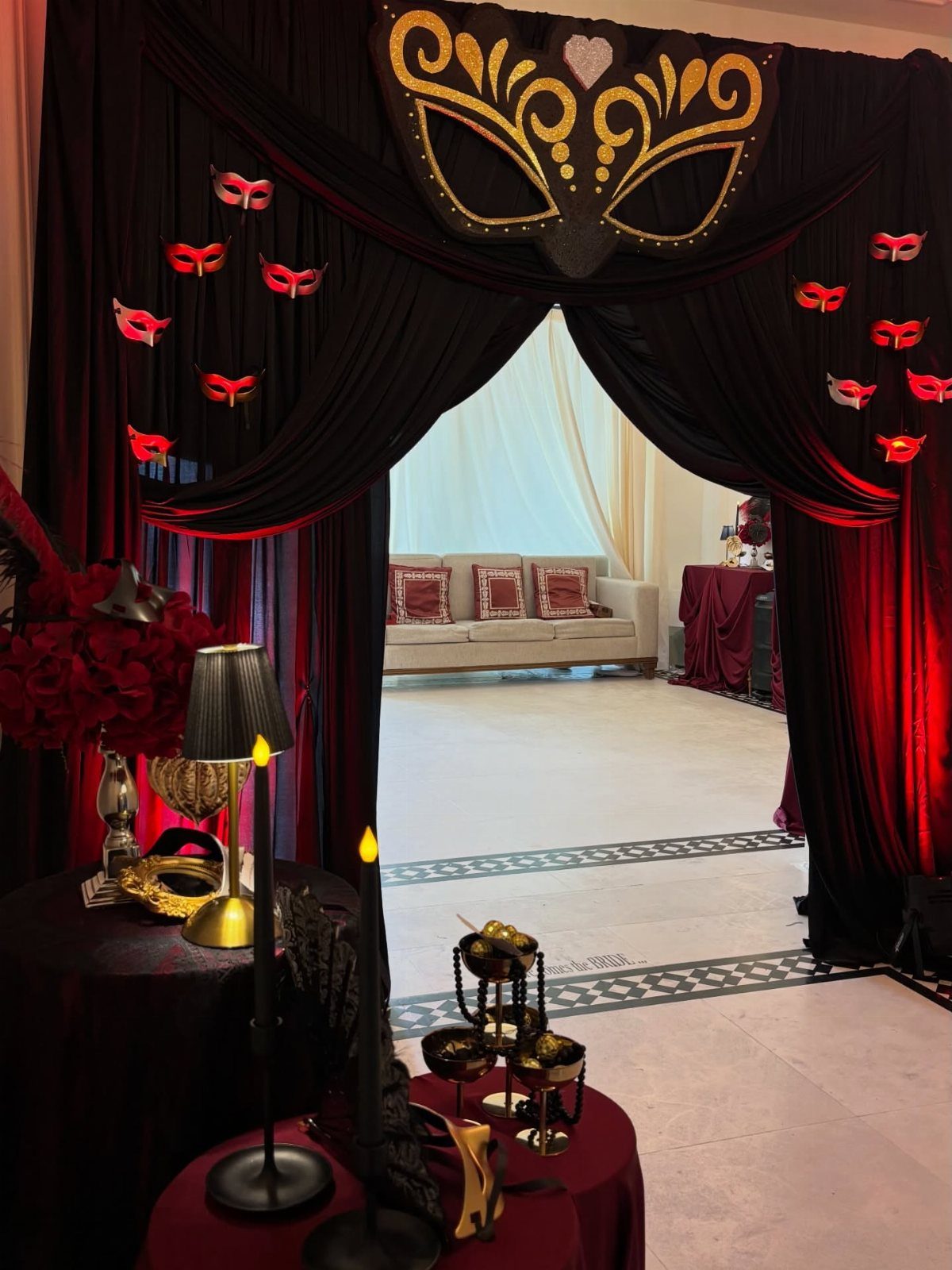 Masquerade party entrance with black and red curtains and gold mask decorations