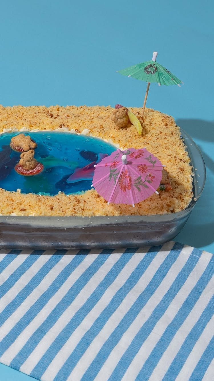 Pool-themed dessert with blue gelatin water, cake crumbs for sand, and cocktail umbrellas.