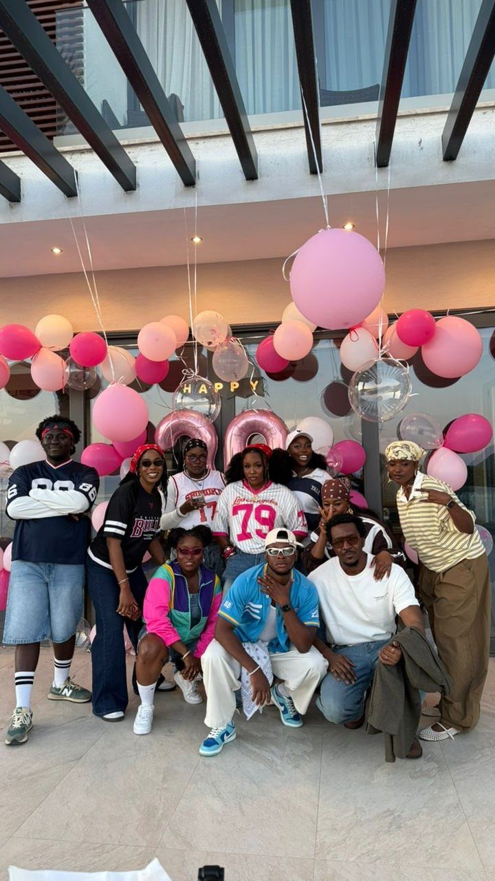 Group of friends posing with pink balloons for a themed birthday celebration.