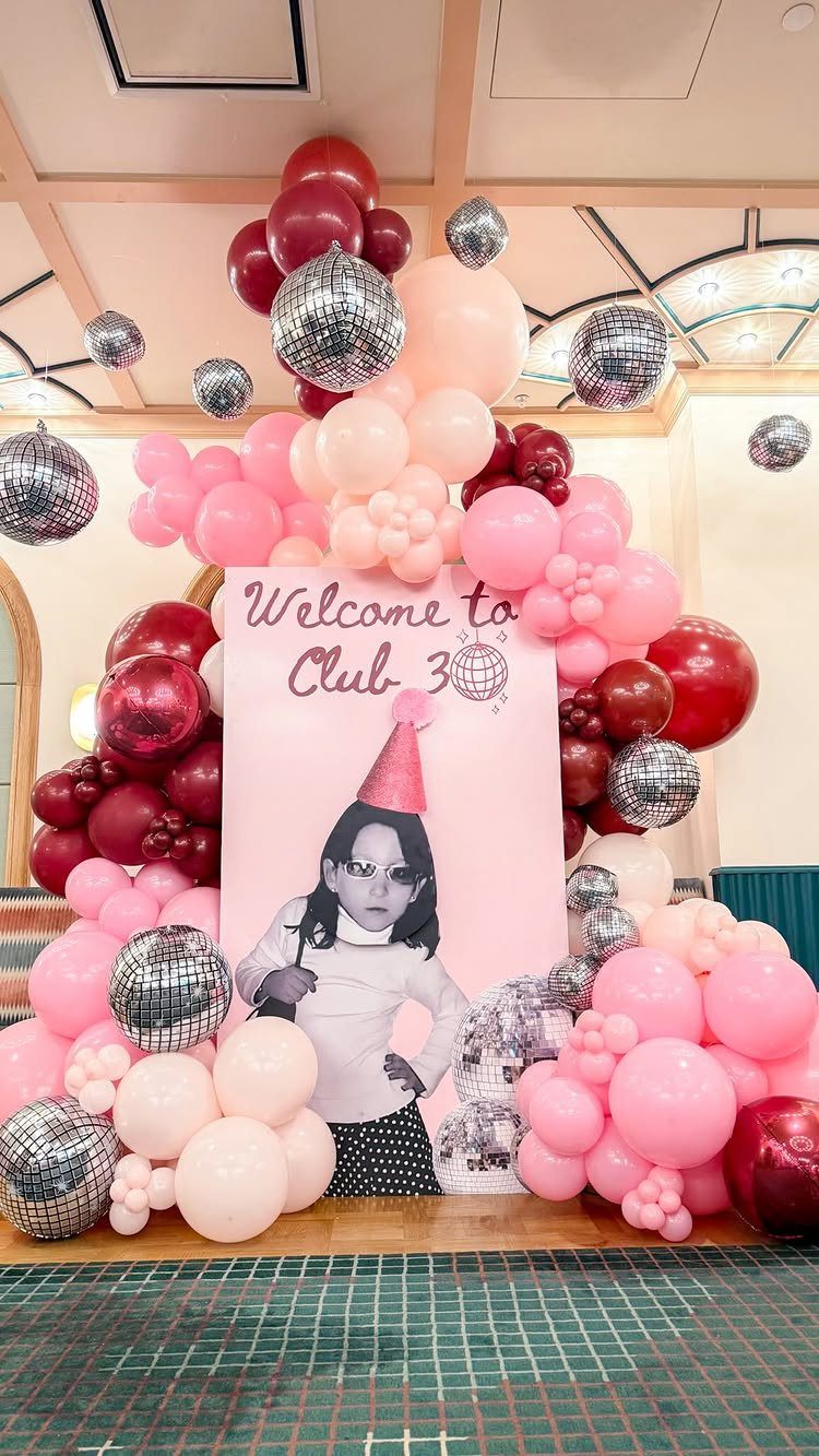 Pink and red balloon arch with disco balls and a Club 30 sign.