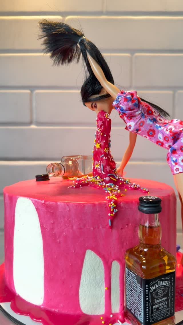Barbie doll face-down in a pink cake next to a miniature whiskey bottle