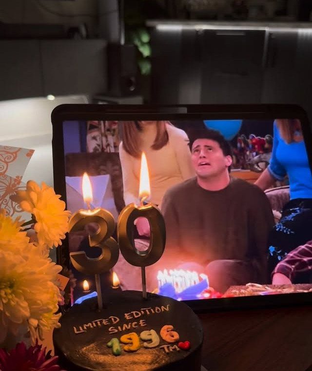 Black birthday cake with gold 30 candles and a tablet showing Friends.
