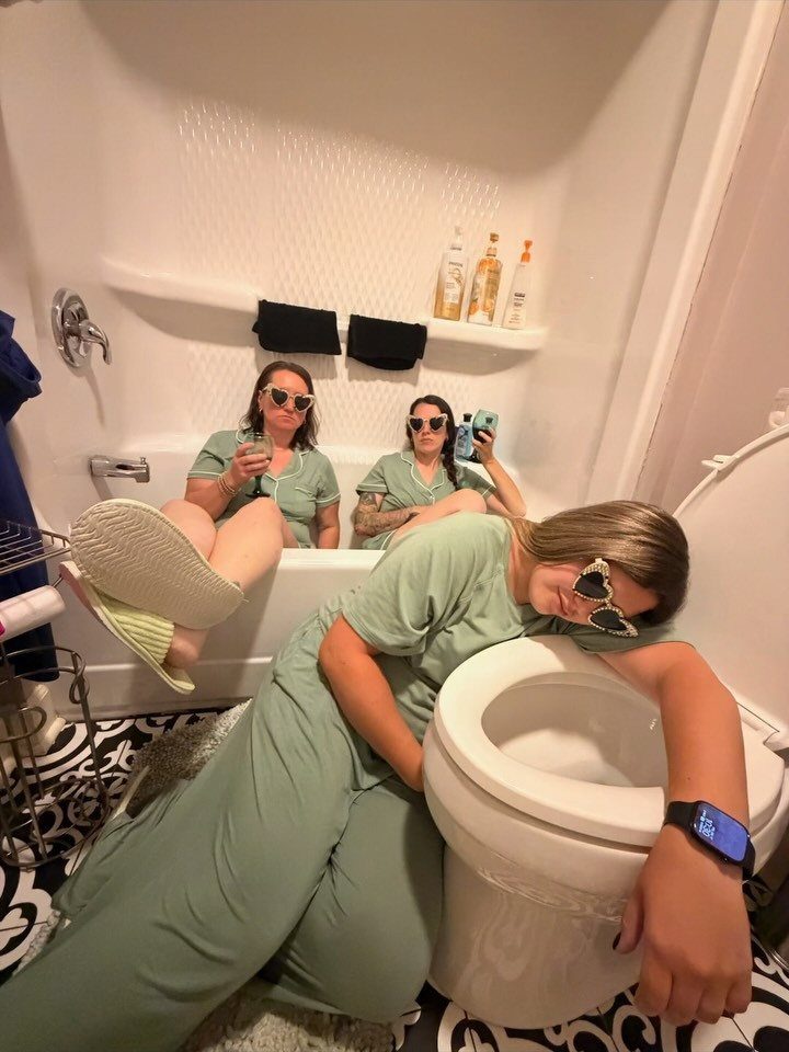 Three women in matching green pajamas posing humorously in a bathroom with a toilet.