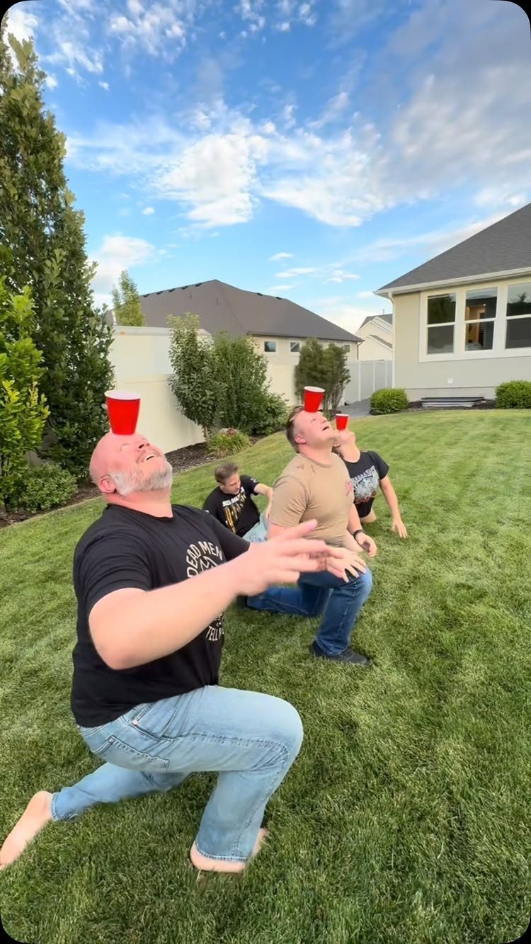 Three men in a backyard balancing red plastic cups on their foreheads.