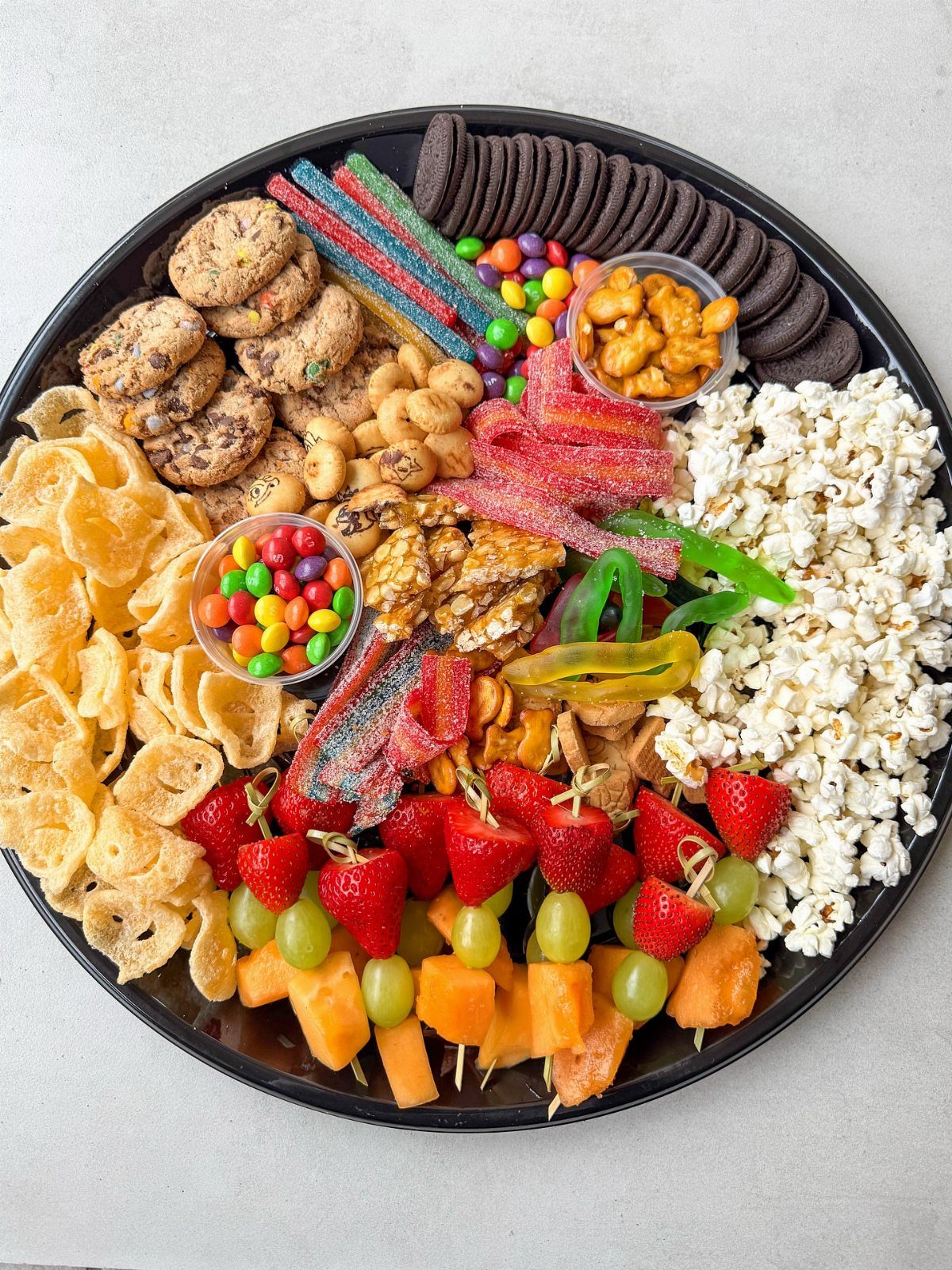 Large black platter filled with assorted snacks, fruits, candies, and savory treats.