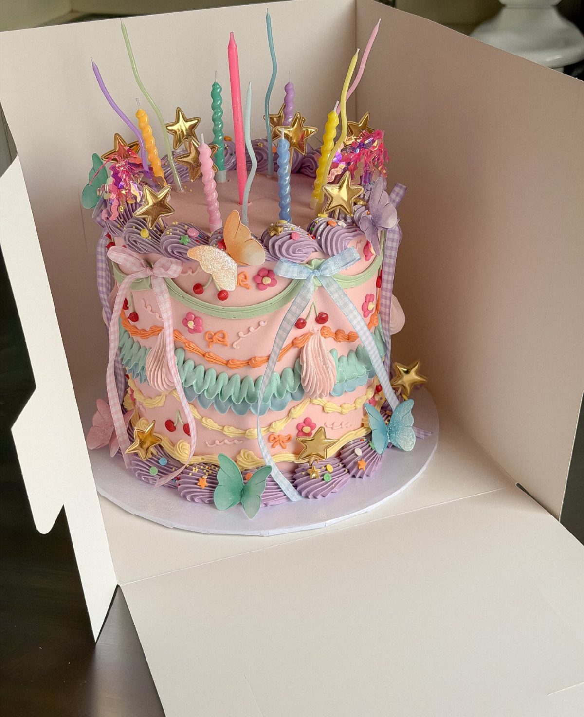 Pink frosted cake with colorful swirls, gold stars, and pastel butterflies in a box.