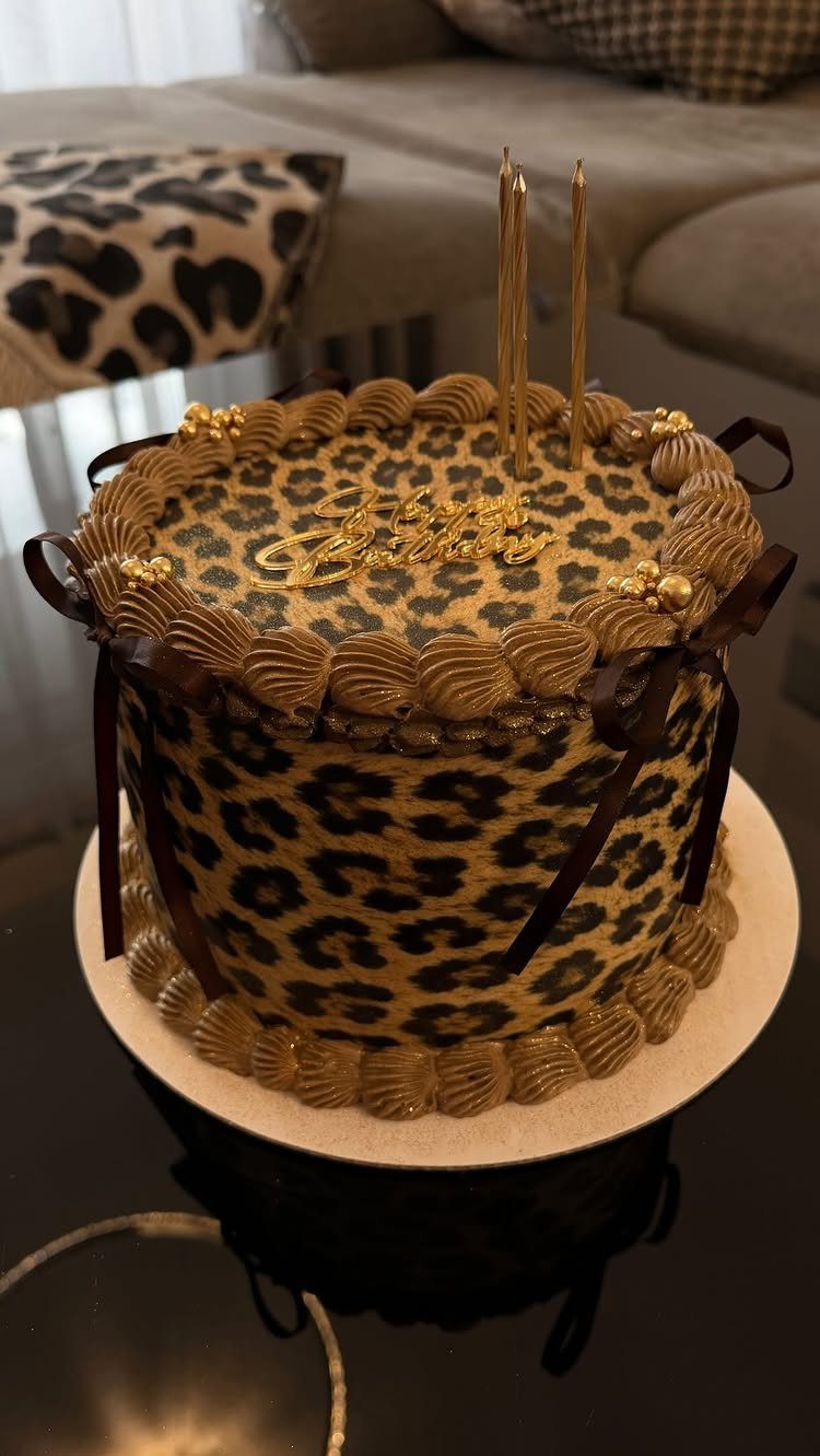 Leopard print cake with gold frosting swirls and gold candles on top.