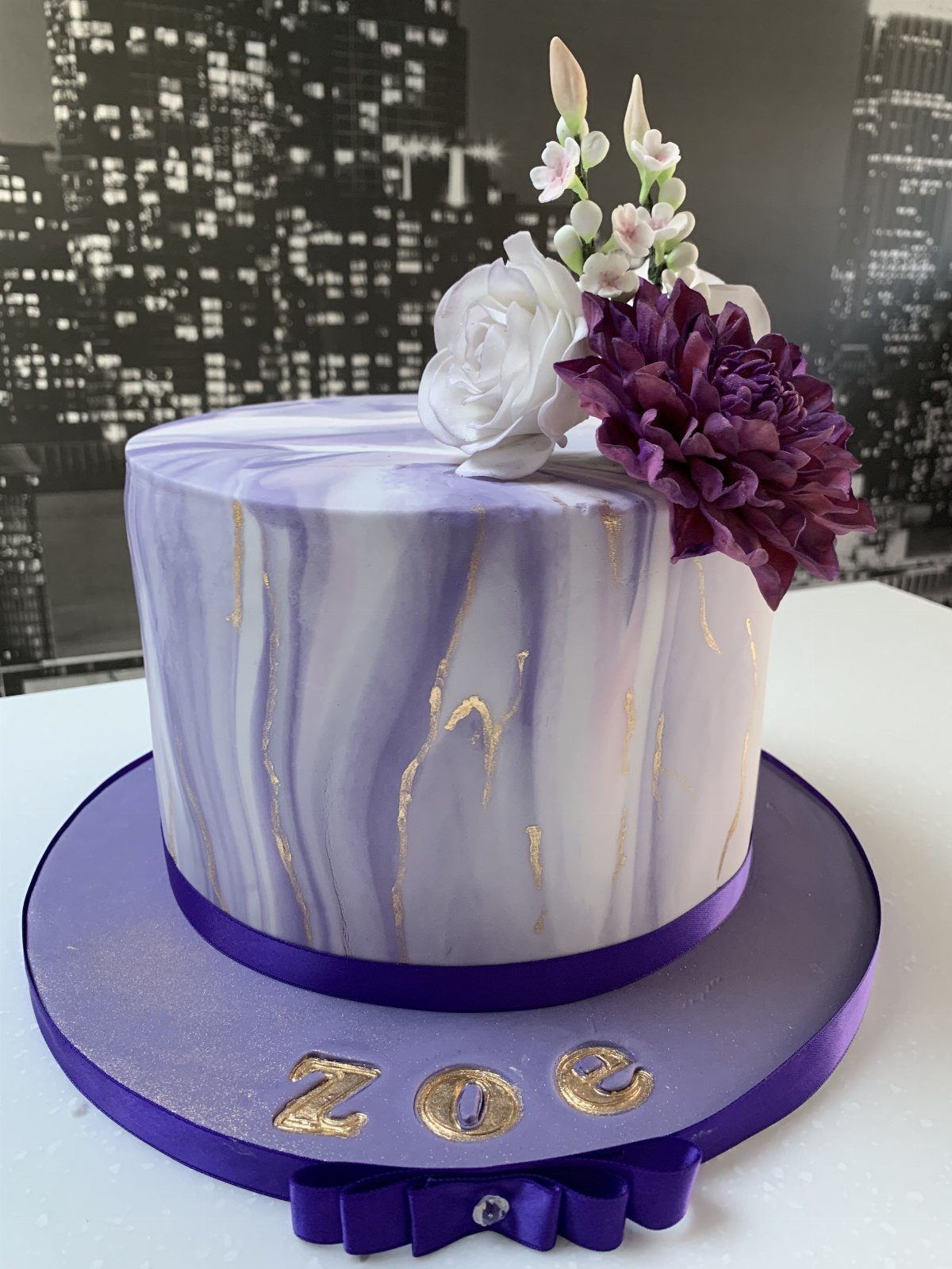 Purple and white marbled fondant cake topped with white and purple flowers.