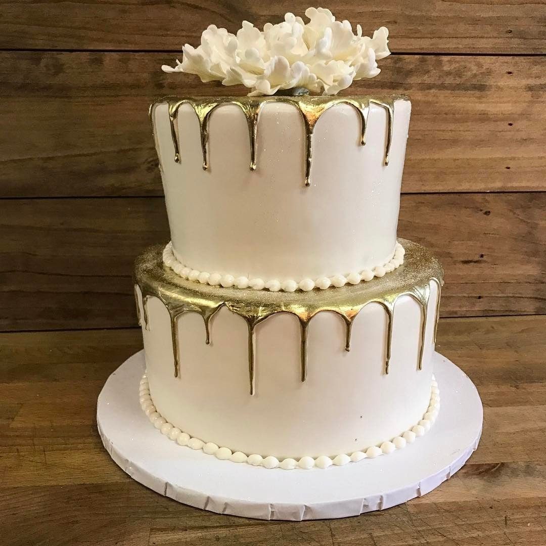 Two-tier white cream cake with gold drip icing and white floral topper.