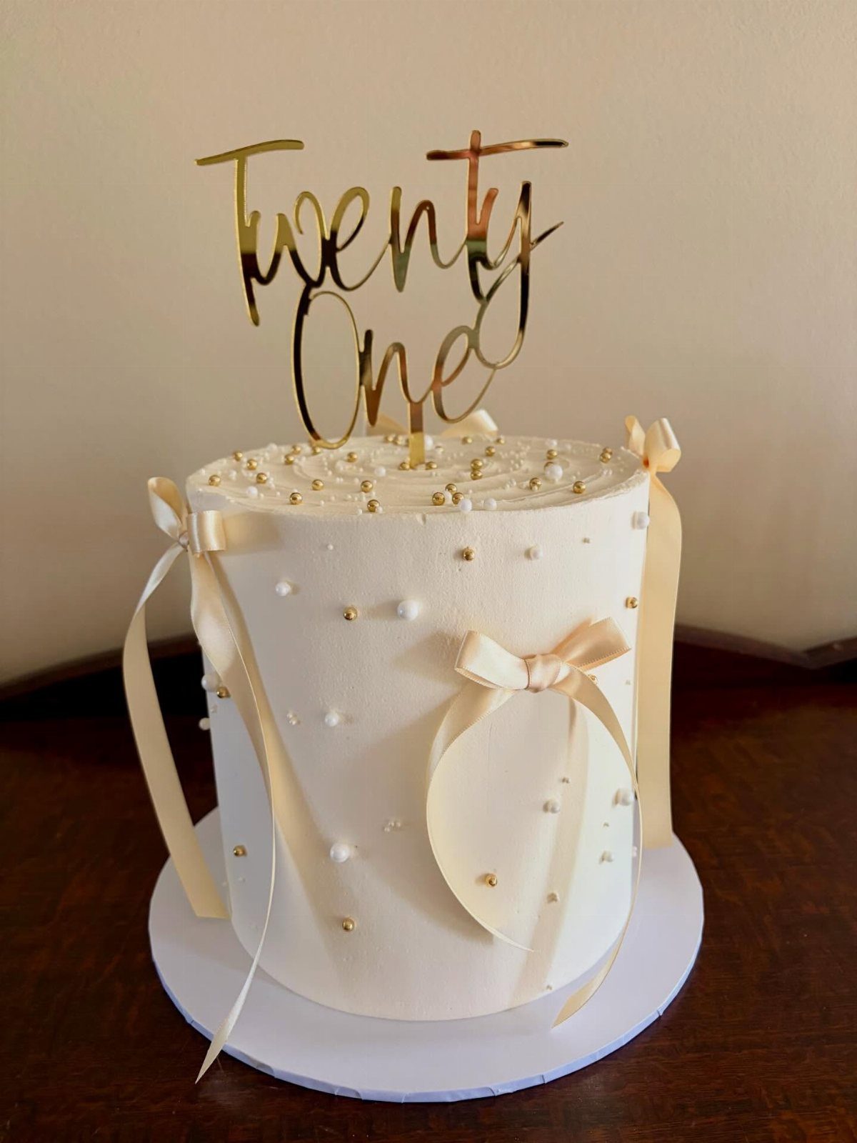 White frosted cake with gold and white pearls and a Twenty One topper