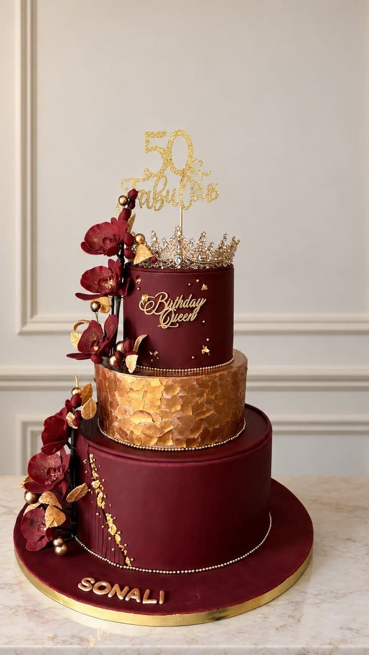 Three-tier burgundy and gold birthday cake with floral accents and a 50 topper.