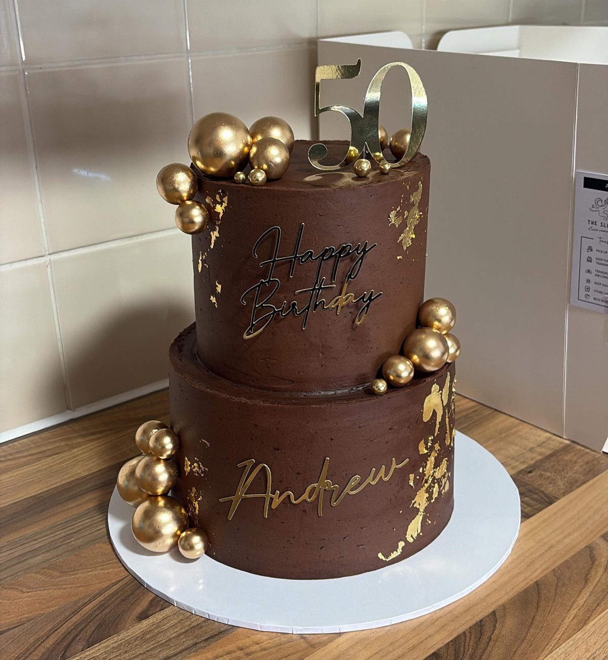 Two-tier chocolate cake with gold leaf, gold spheres, and a gold 50 topper.