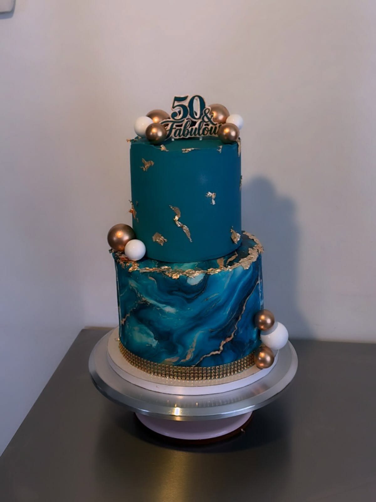 Two-tier teal and gold birthday cake with marble effect and 50 Fabulous topper