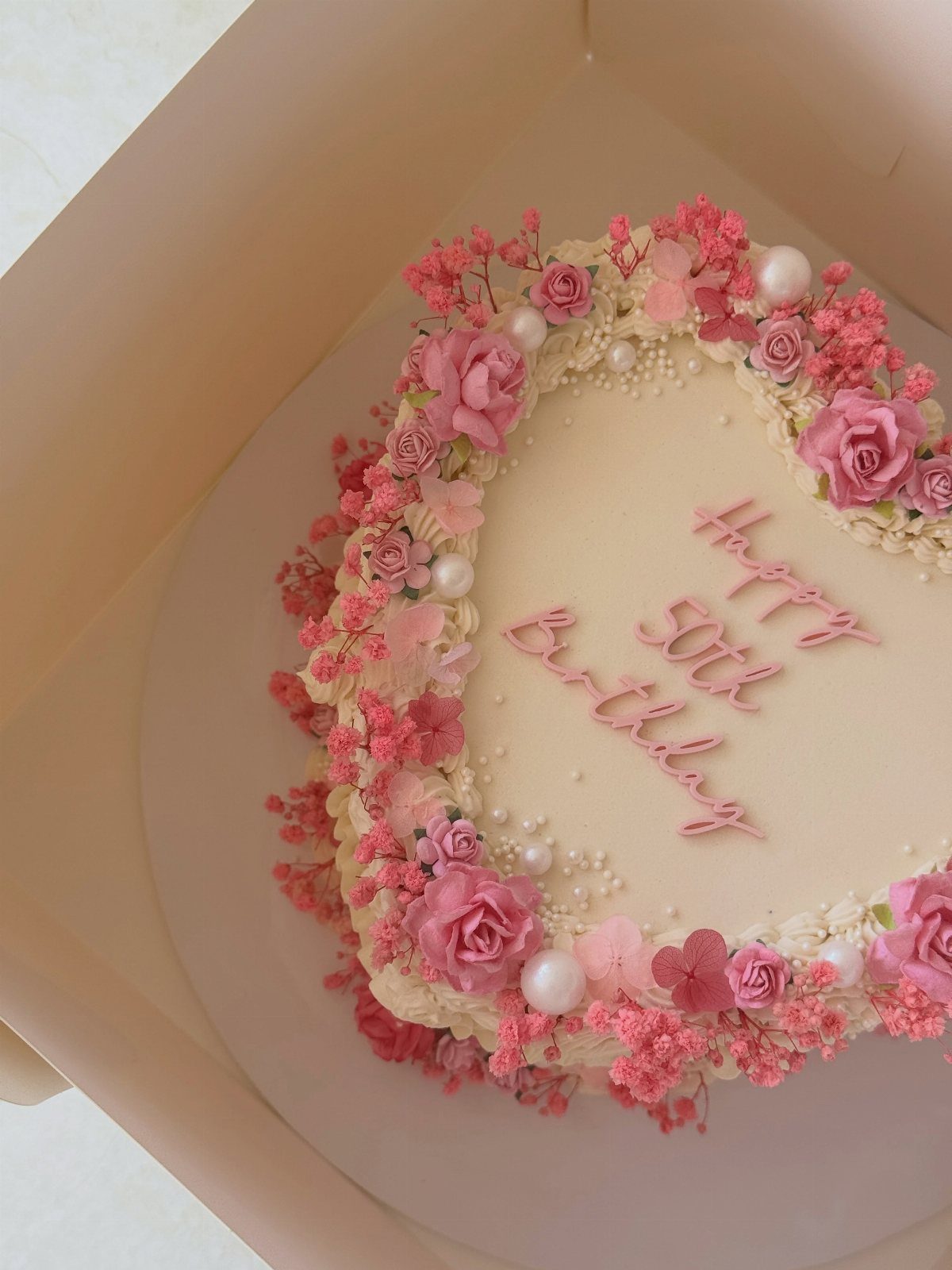 Heart-shaped white cake with pink buttercream roses and Happy 50th Birthday text.
