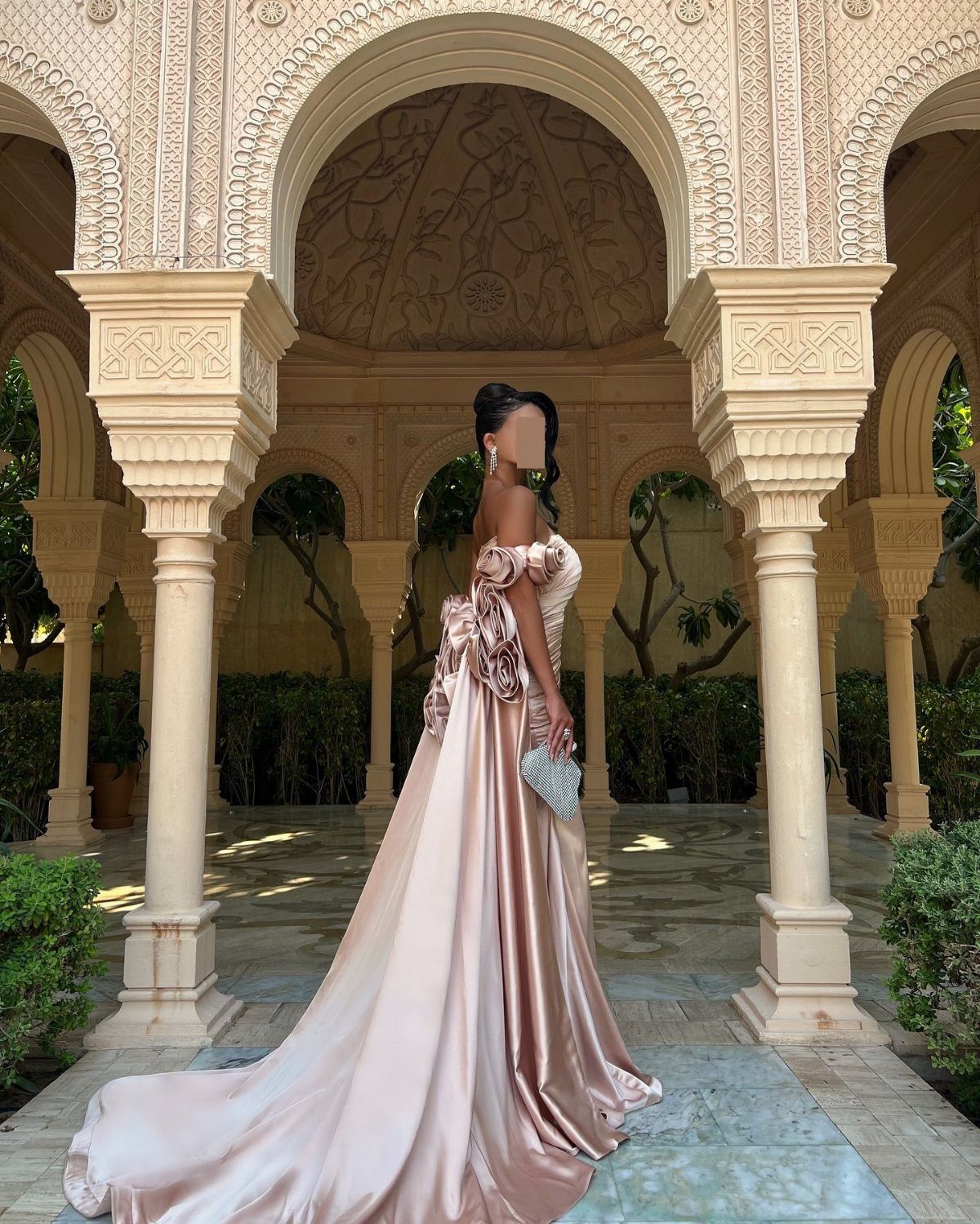 Woman in a champagne-gold satin gown with 3D rose petal appliqués standing under arches.
