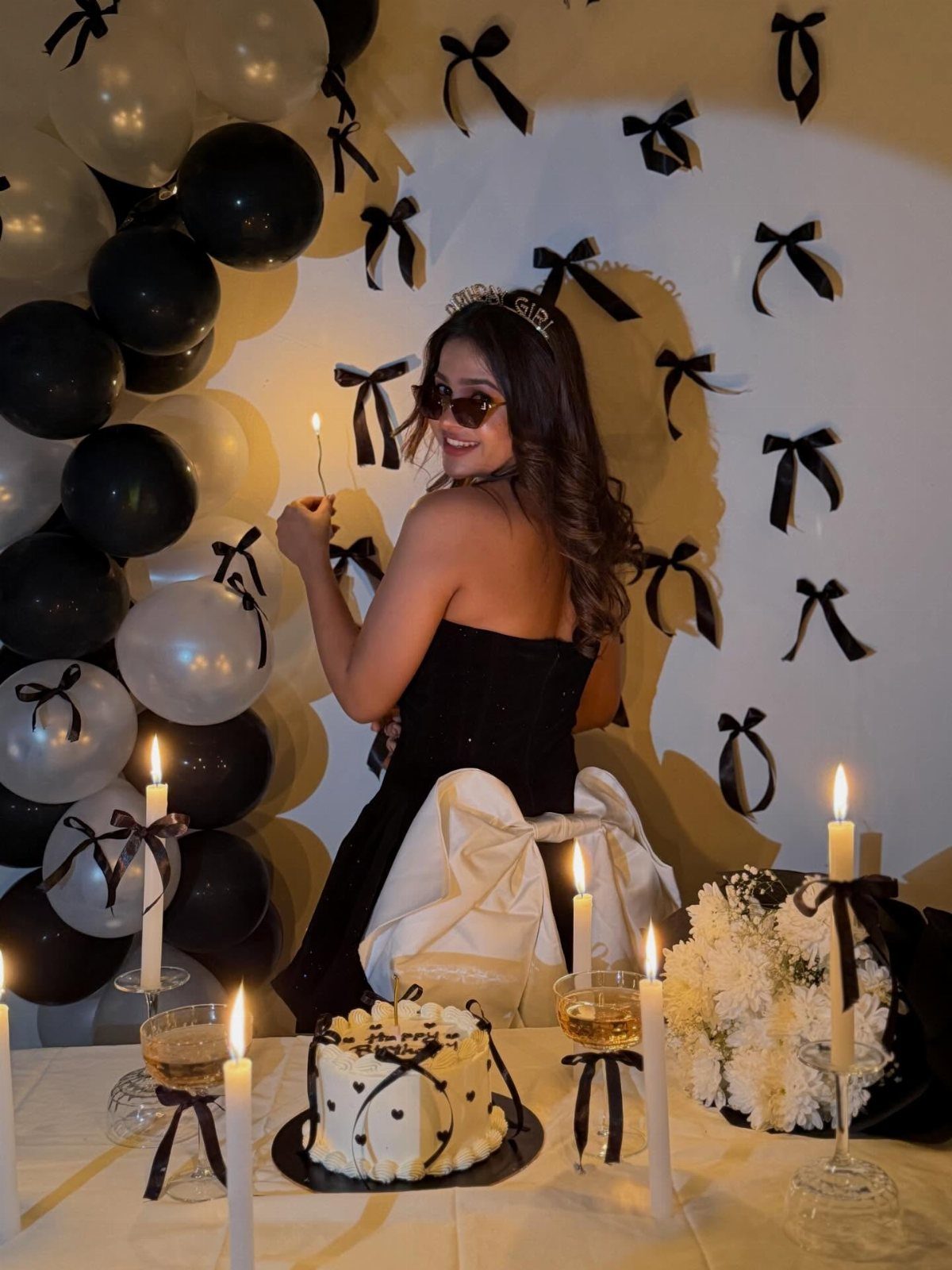 Woman in a strapless black dress posing with black and white birthday decorations.