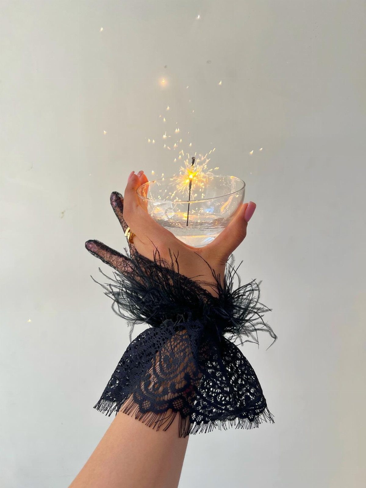 Hand in black lace glove holding a glass bowl with a lit sparkler
