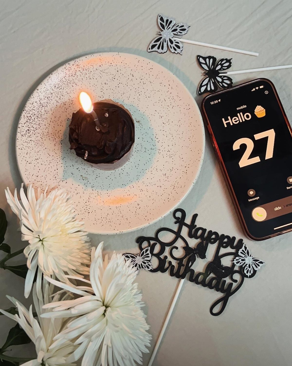 Chocolate cupcake with a lit candle on a plate next to white flowers.