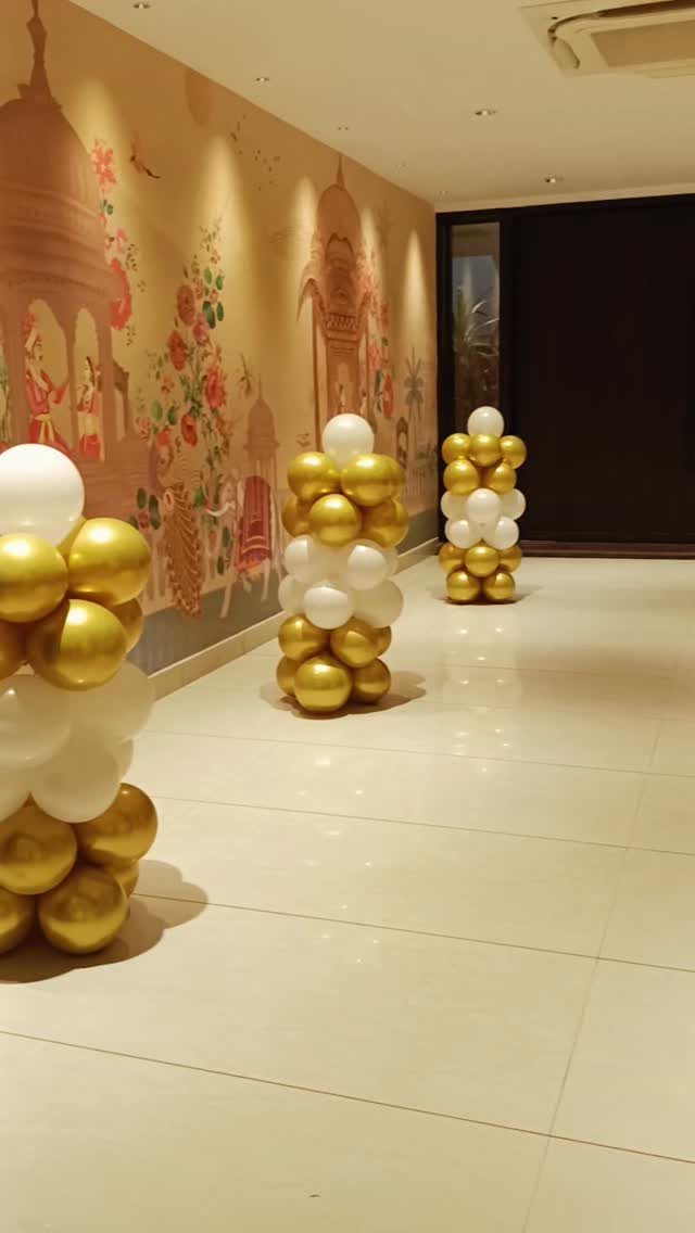 Gold and white balloon columns standing in a room with a mural wall.