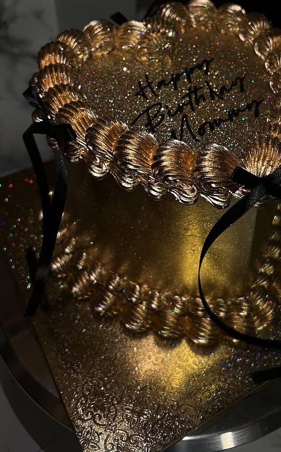 Gold glitter cake with ornate frosting and black ribbons for a birthday celebration