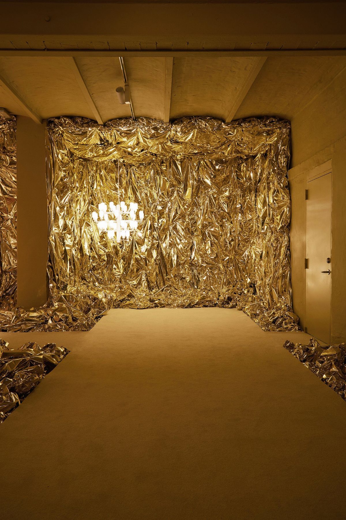 Crinkled gold foil reflective backdrop with a glowing chandelier in a room.