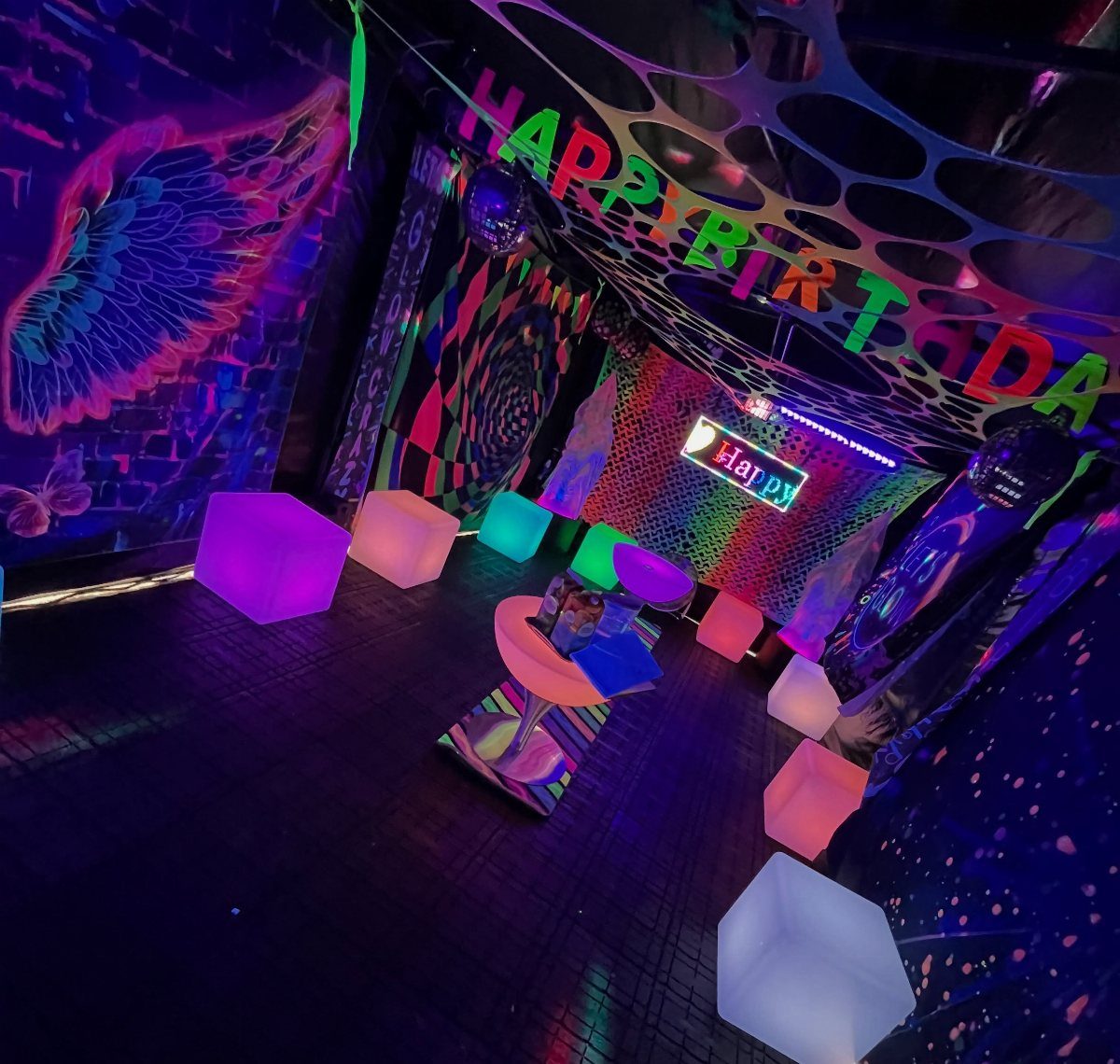 Neon birthday party room with glowing cube seats and black light decorations.