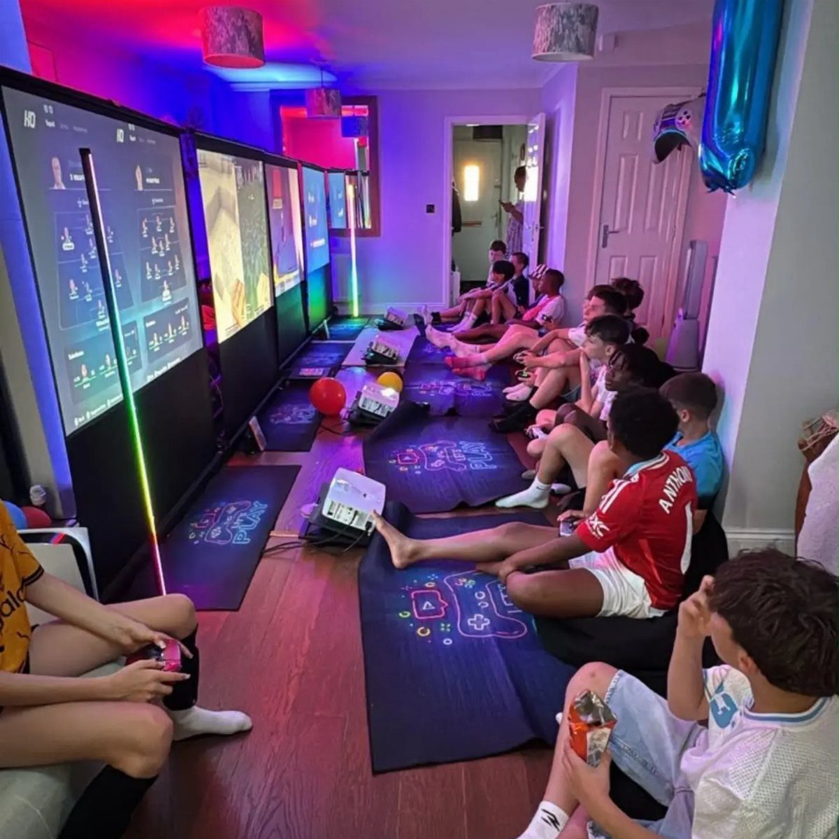 Teenage boys sitting on floor mats playing video games on large vertical screens.
