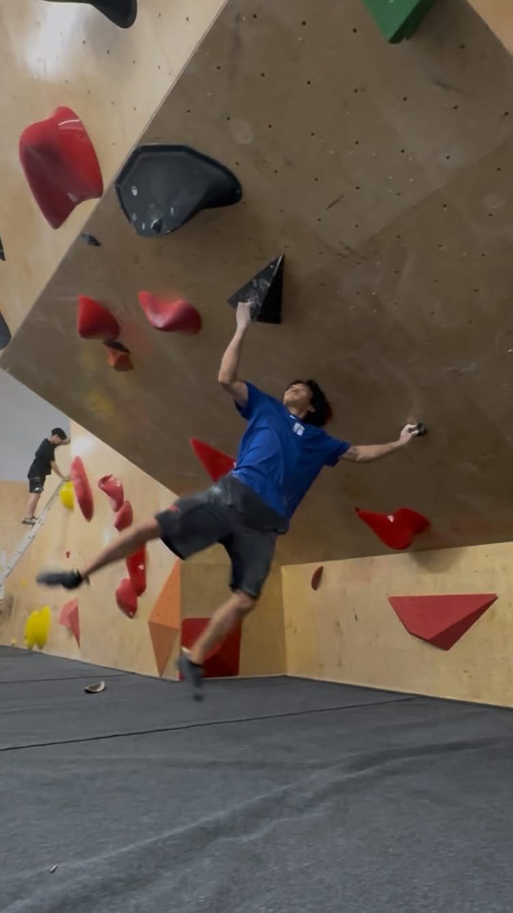 Young man climbing a wooden indoor bouldering wall with colorful climbing holds.