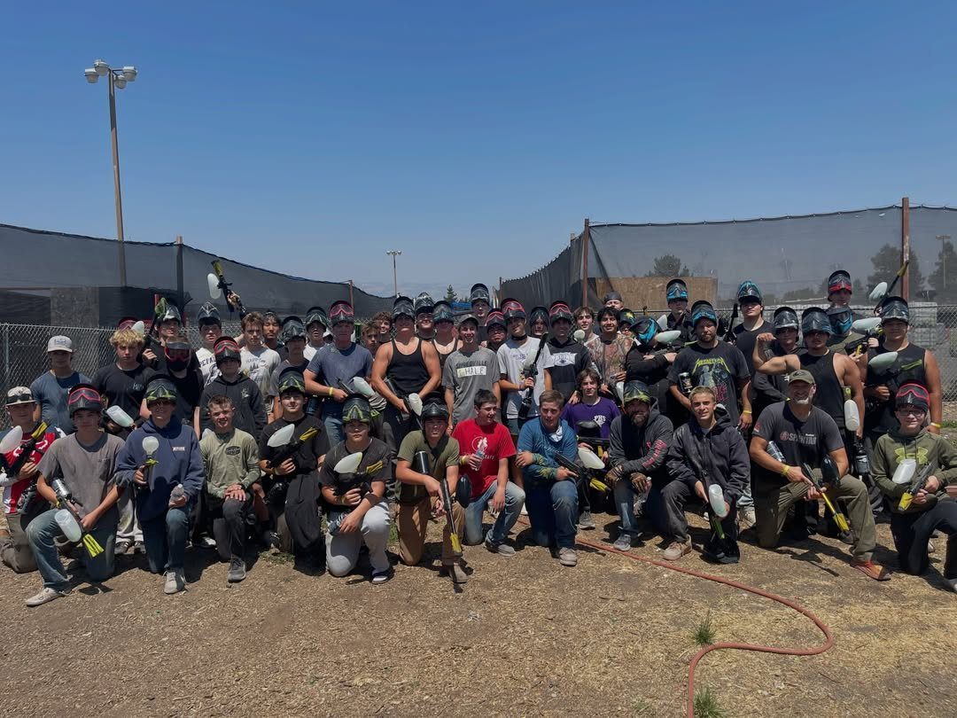 Group of teenage boys holding paintball markers and wearing masks on a field.