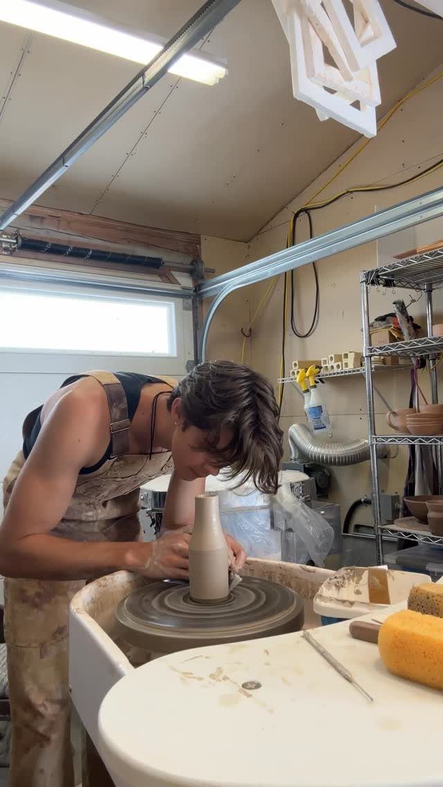 Young man shaping a clay vase on a pottery wheel in a garage studio