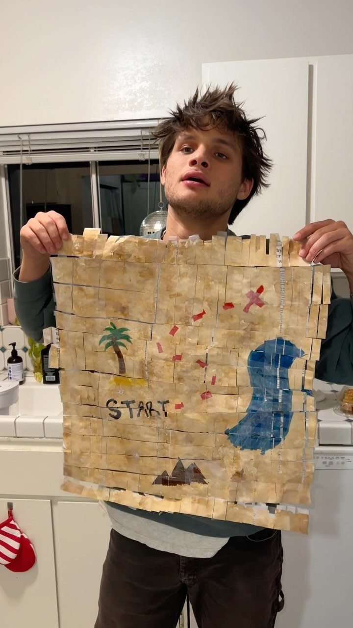 Young man holding a handmade treasure map with a start point and landmarks.