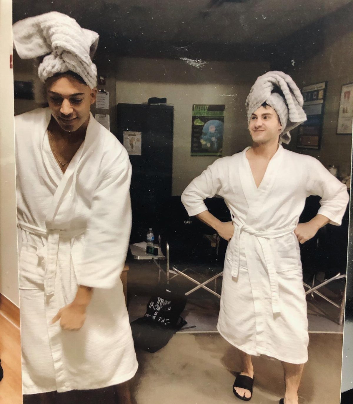 Two young men wearing white bathrobes and towel head wraps posing together.