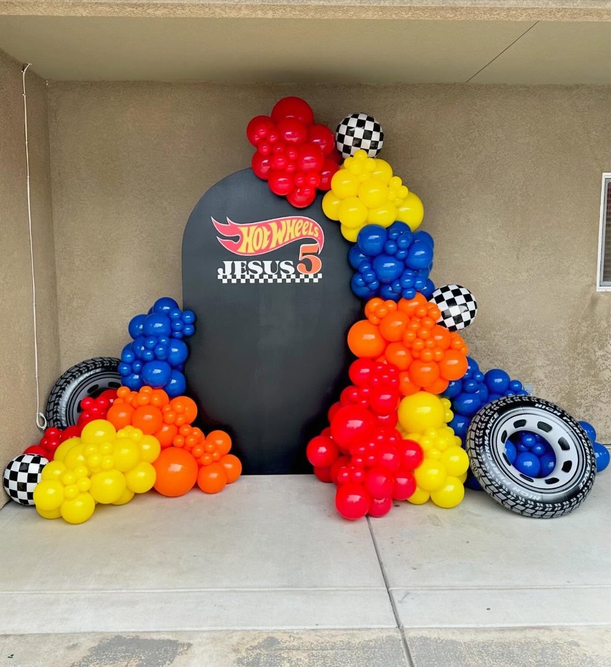Hot Wheels party backdrop with colorful balloon garland and large toy tires.