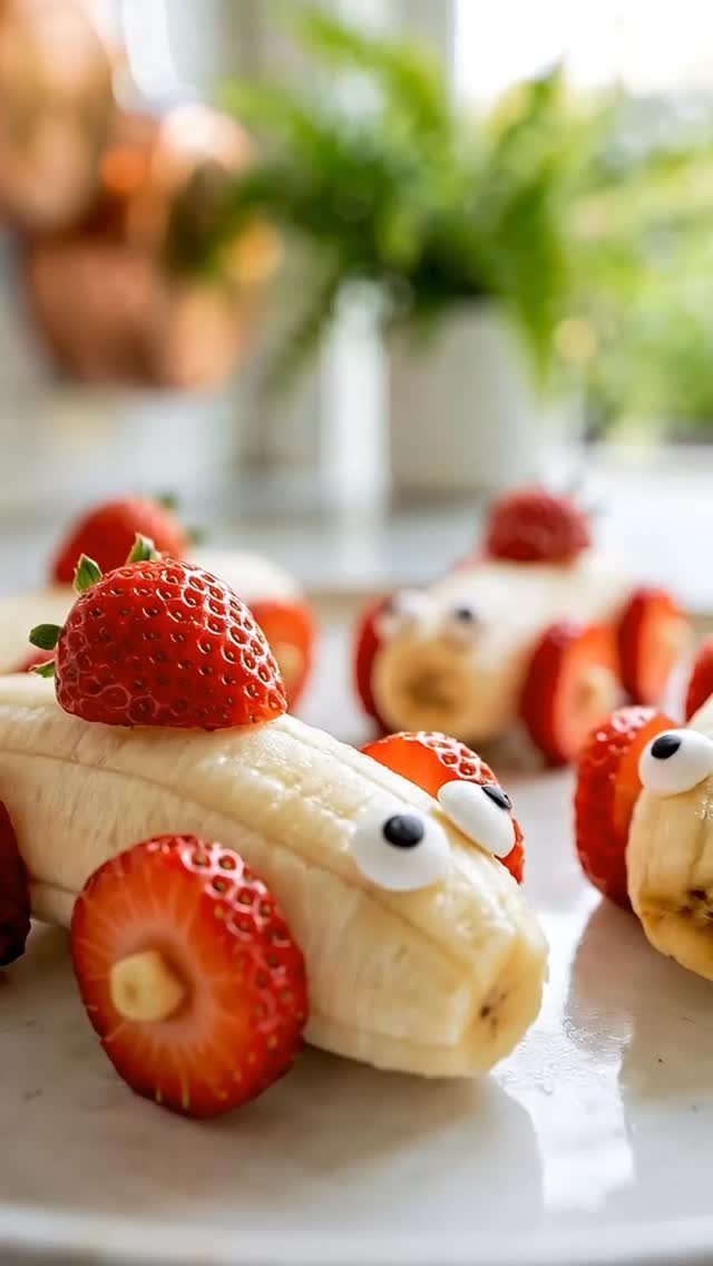 Banana and strawberry fruit cars with candy eyes on a white plate
