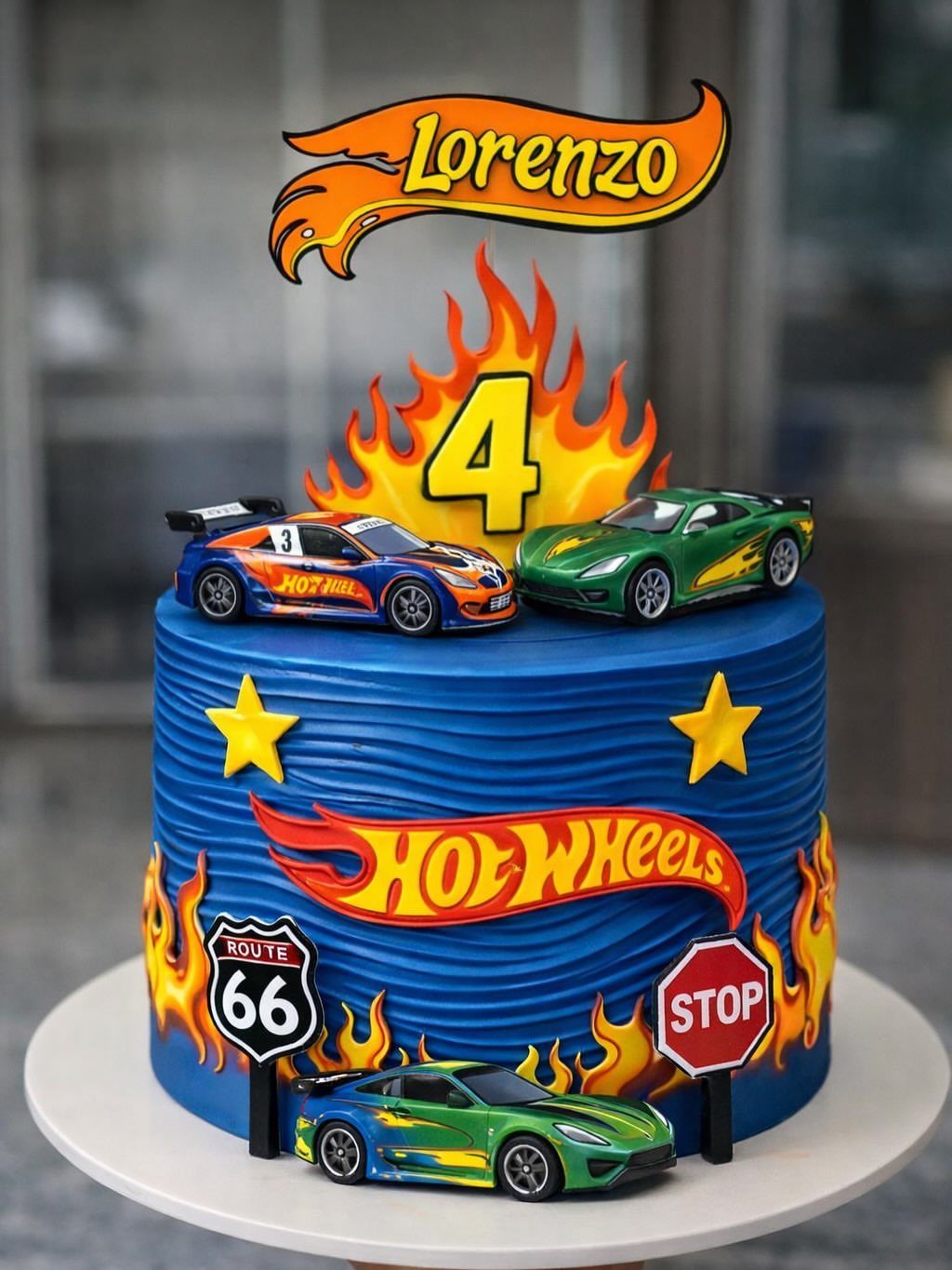 Blue Hot Wheels birthday cake decorated with toy cars, flames, and a number 4 topper.