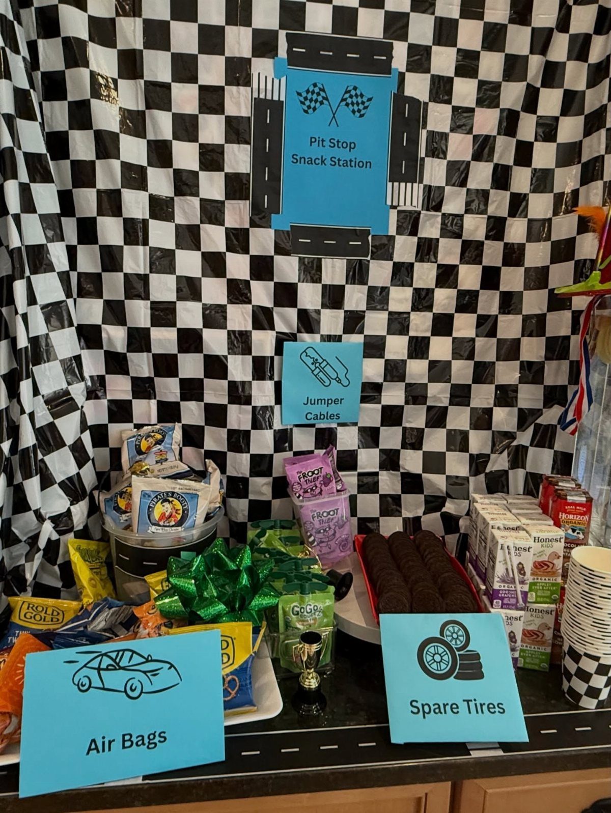 Car themed snack station with checkered backdrop and funny automotive food labels