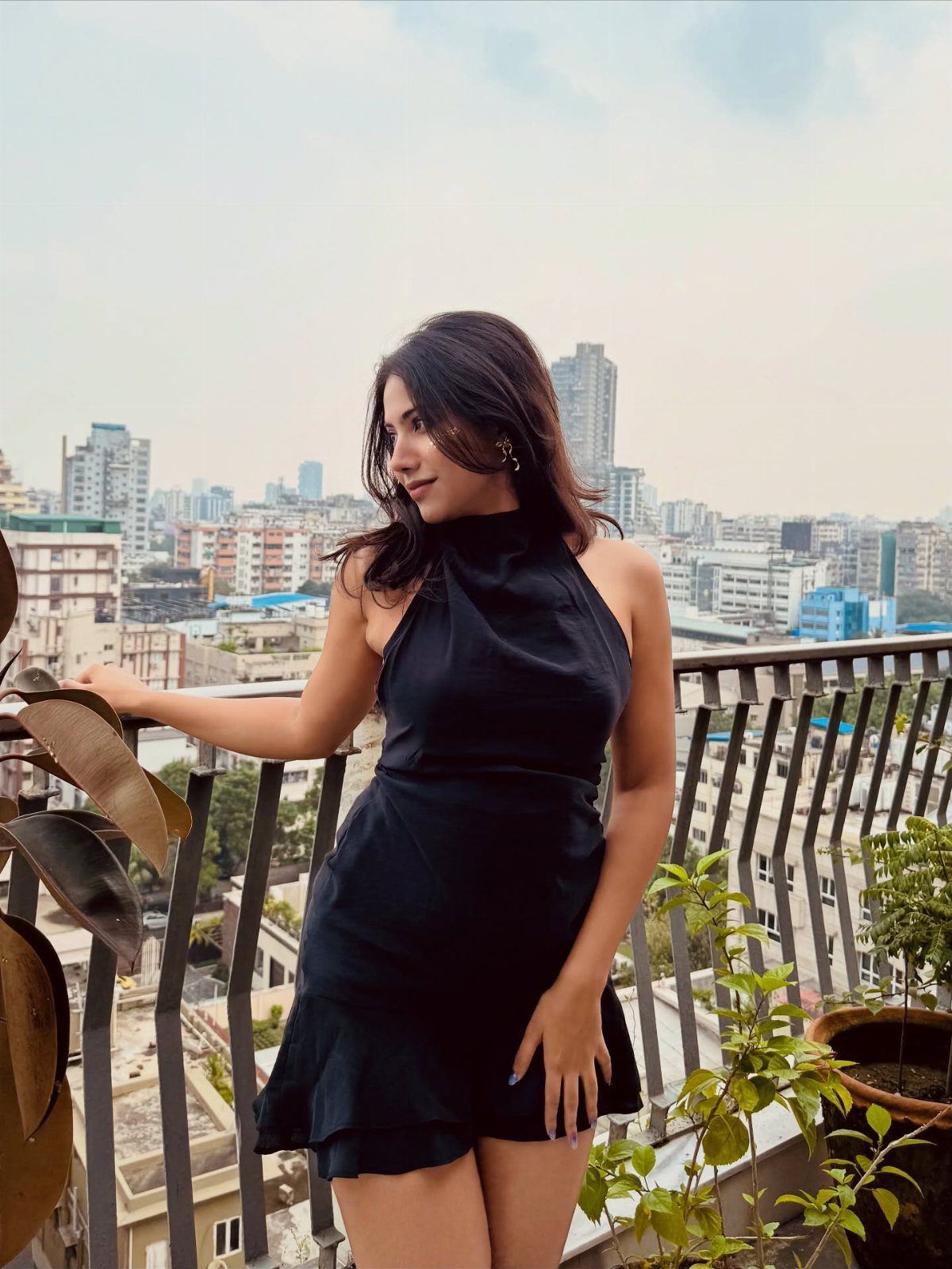 Woman in a short black halter-neck dress posing on a city balcony.