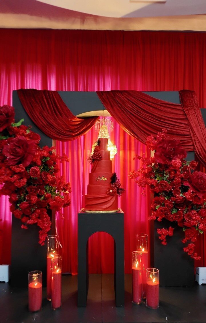 Red tiered cake and red roses set against red and black curtains.