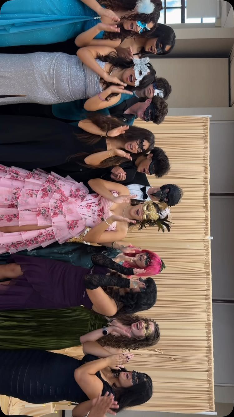 Group of people in formal dresses and masquerade masks posing before a curtain.
