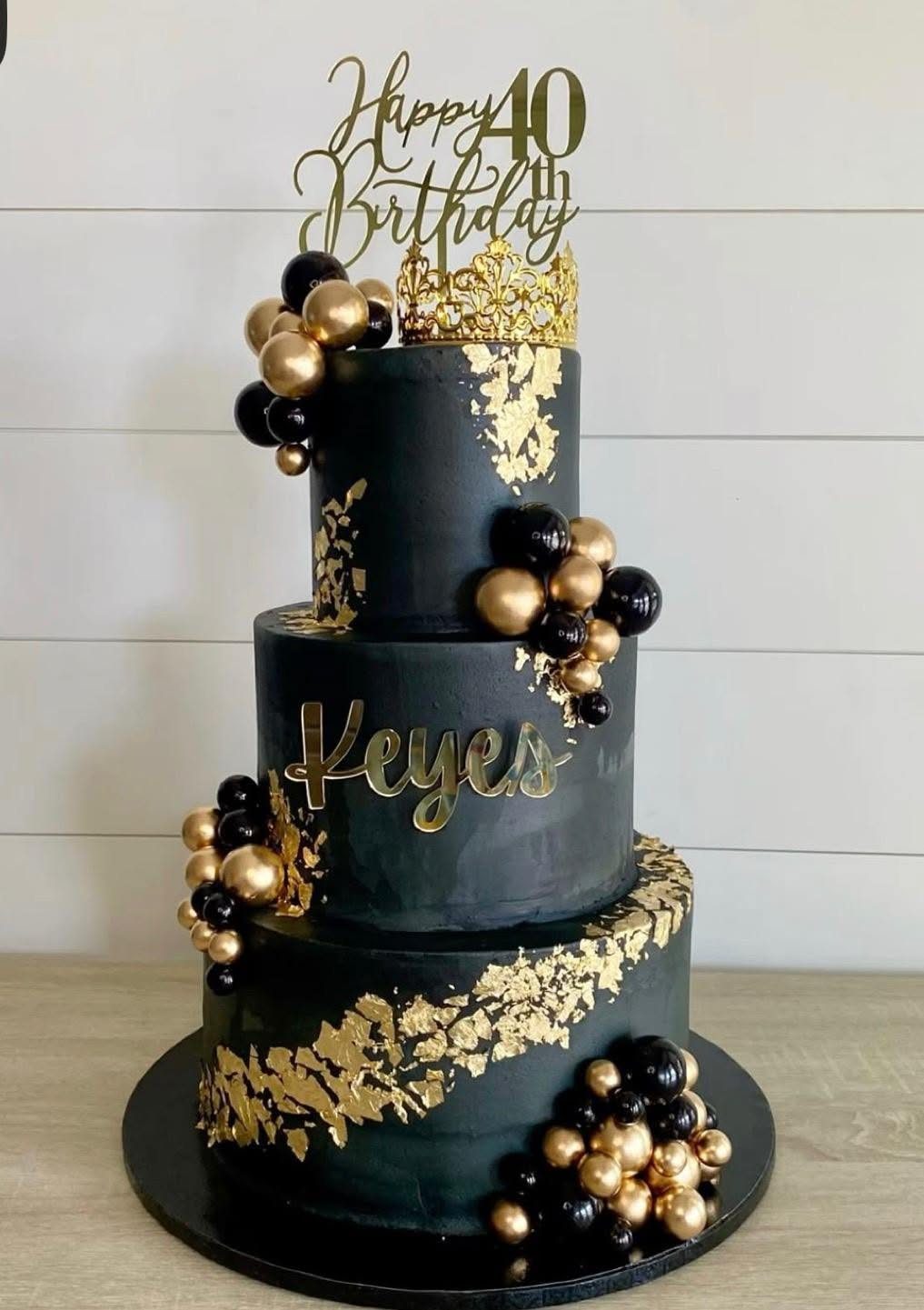 Three-tiered black cake with gold leaf, gold ornaments, and a 40th birthday topper.